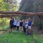 Smiling hiking group pausing for a photo under a giant fallen tree deep in the forests of Nacka Nature Reserve near Stockholm.