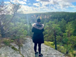 Eine Frau genießt einen malerischen Aussichtspunkt mit Blick auf einen endlosen Kiefernwald. Ein friedlicher Moment während einer geführten Wanderung in der Nähe von Stockholm.