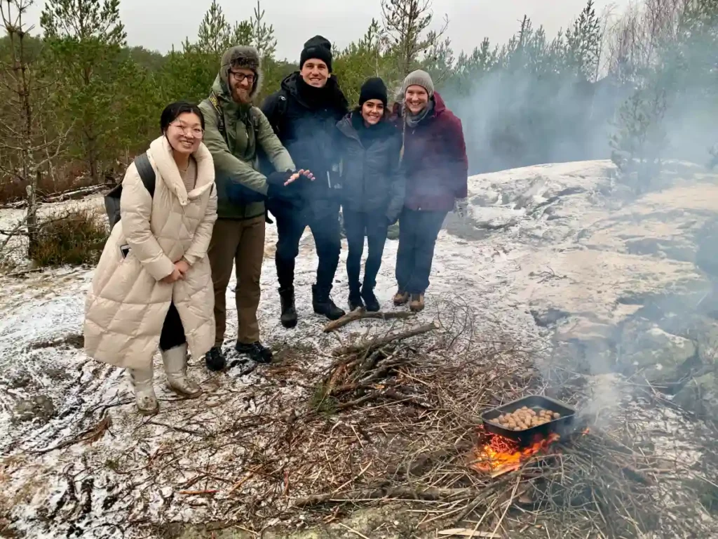Eine Gruppe von Kunden genießt eine Mahlzeit am Lagerfeuer während einer Winterwanderung in der Nähe von Stockholm