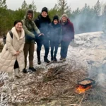 Eine Gruppe von Kunden genießt eine Mahlzeit am Lagerfeuer während einer Winterwanderung in der Nähe von Stockholm