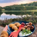Comida tradicional sueca con albóndigas, patatas, arándanos rojos y cebollino, degustada junto a un lago durante una excursión guiada al atardecer en el Parque Nacional de Tyresta.
