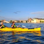Dos remeros disfrutan del cálido resplandor del atardecer mientras navegan en kayak por las vías fluviales del centro de Estocolmo.
