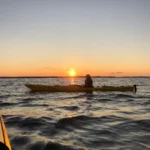 Kajakpaddling i solnedgången på öppet vatten med gyllene ljus som reflekterar över skärgården.
