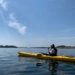 En paddlare njuter av vida vyer och lugna vatten i skärgården en varm kväll.