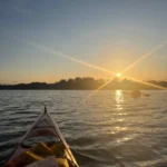 Solnedgångens ljus skiner över havet med en kajak på väg mot den gyllene horisonten.