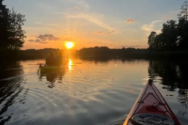 Two people paddling into a glowing sunset with trees and still water all around.