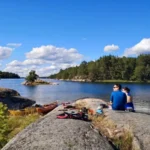Ett par njuter av en naturskön picknick på en klippö efter en dag med kajakpaddling i Stockholms skärgård.