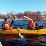 Dos kayakistas remando en invierno por aguas azules rodeadas de árboles nevados durante una excursión en kayak en Estocolmo.