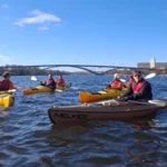 Grupo de kayakistas disfrutando de un fresco día de invierno en el agua en Estocolmo, con cielos azules despejados. Una aventura urbana pintoresca y refrescante.