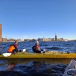 Dos kayakistas abrigados disfrutan de las vistas del casco antiguo de Estocolmo desde el agua durante una soleada y fría excursión invernal.