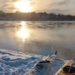 Puesta de sol sobre una costa helada con kayaks descansando en la nieve: el mágico final de una aventura invernal a remo en Estocolmo.