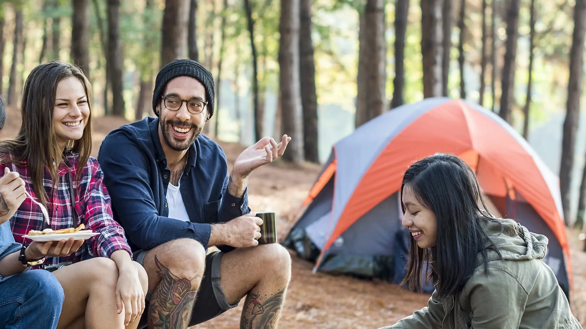 Eine Gruppe glücklicher Camper sitzt an einem Zelt im Wald und genießt Kaffee und Essen während eines Campingausflugs mit Leihausrüstung in Stockholm